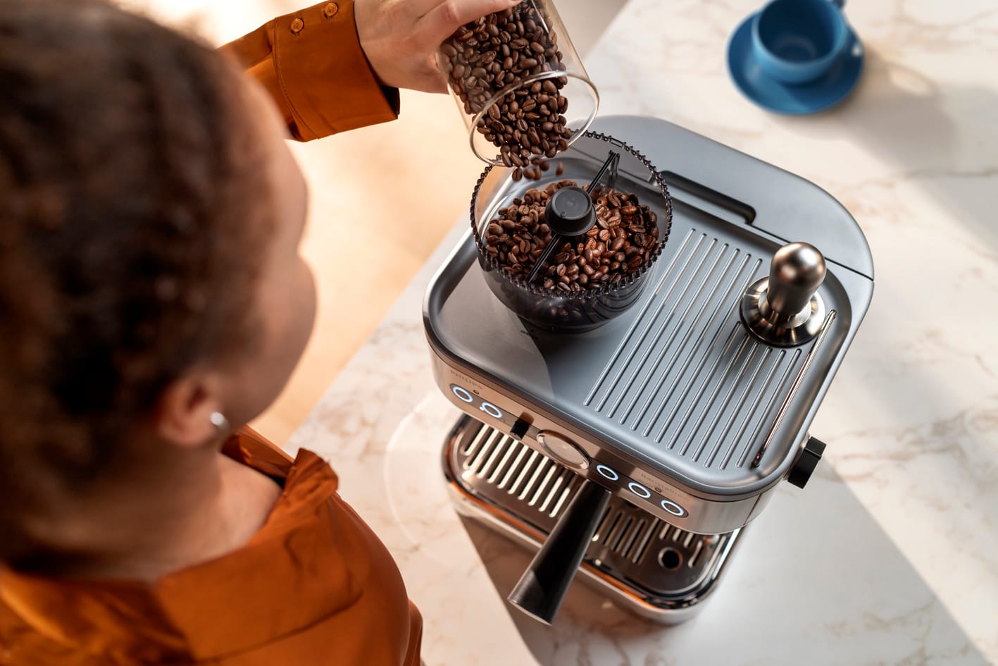 Una joven vierte granos de caf&eacute; en el contenedor de granos de caf&eacute; Barista Brew de Philips