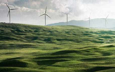 Una fotografía de una ladera verde con turbinas eólicas girando para crear energía renovable.
